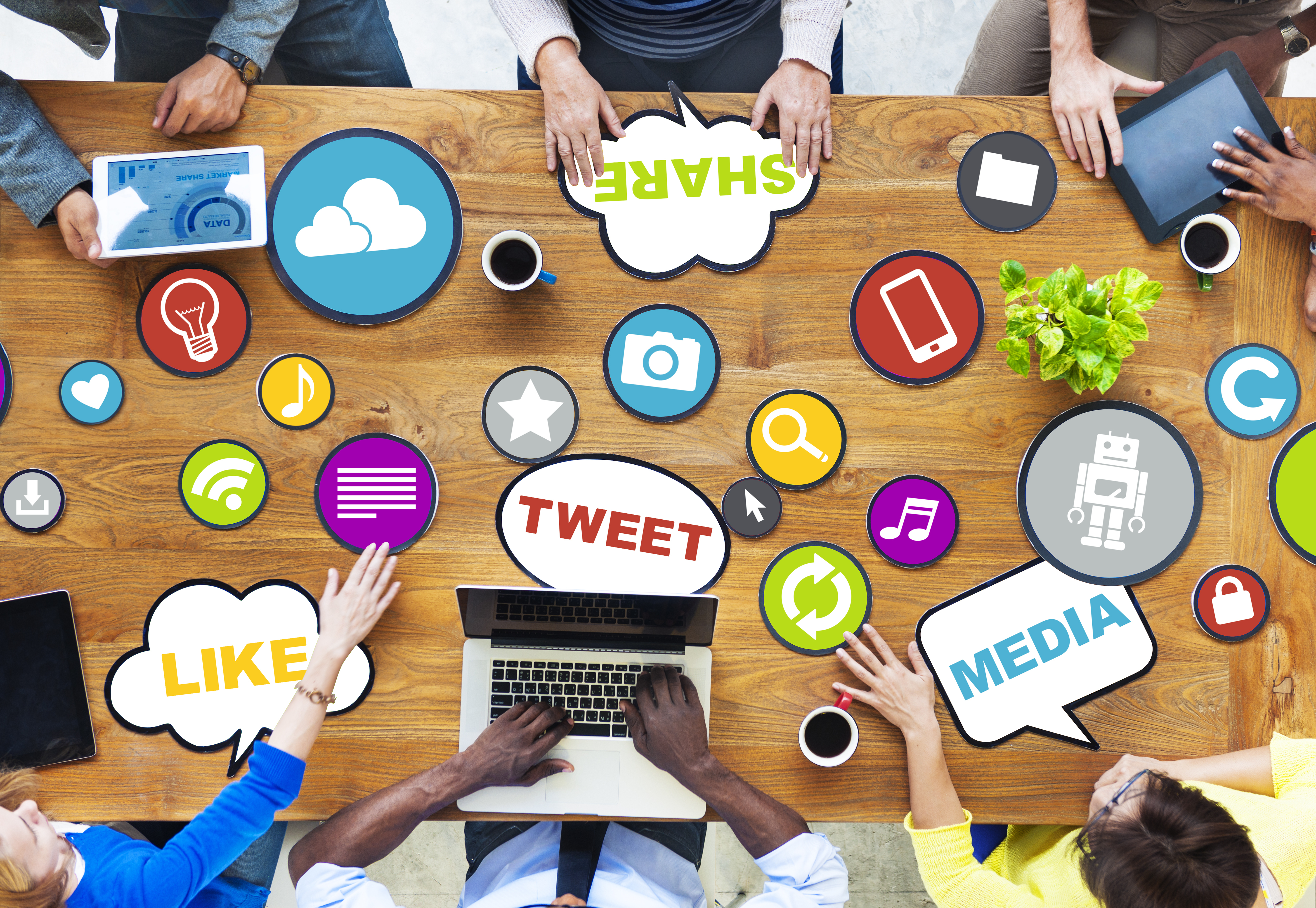 a group of six people working with colorful placards containing images related to social media such as a camera, lightbulb, battery, cloud, and the words tweet, share, media, and like.